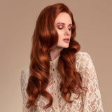 Female model with flowing long red wavy hair from using Moo and Yoo Miracle Conditioner. She has pale skin and a pale cream lacey top on.  She is looking to the right so you can see the full side of her hair. She has super shiny long wavy hair using Moo and Yoo conditioner with lots of volume.