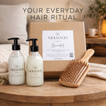 A hair care gift set on a wooden tray, featuring two frosted pump bottles of Moo & Yoo Miracle Shampoo and Miracle Conditioner, a brown kraft box with a white label, and a wooden hairbrush. The background shows a cozy bedroom setting with a bed and a lamp, and the text 'YOUR EVERYDAY HAIR RITUAL' is displayed at the top.