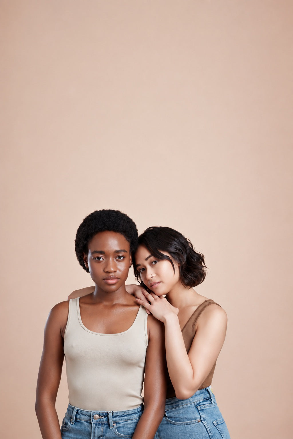 Two women with different hair types and skin tones standing together, showcasing healthy, naturally shiny hair against a soft neutral background