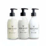 Three glass bottles of Moo and Yoo products sitting side by side. It is a Miracle Shampoo, Conditioner and Miracle Milk leave-in conditioner. They are on a white background