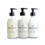 Three glass bottles of Moo and Yoo products sitting side by side. It is a Miracle Shampoo, Conditioner and Miracle Milk leave-in conditioner. They are on a white background