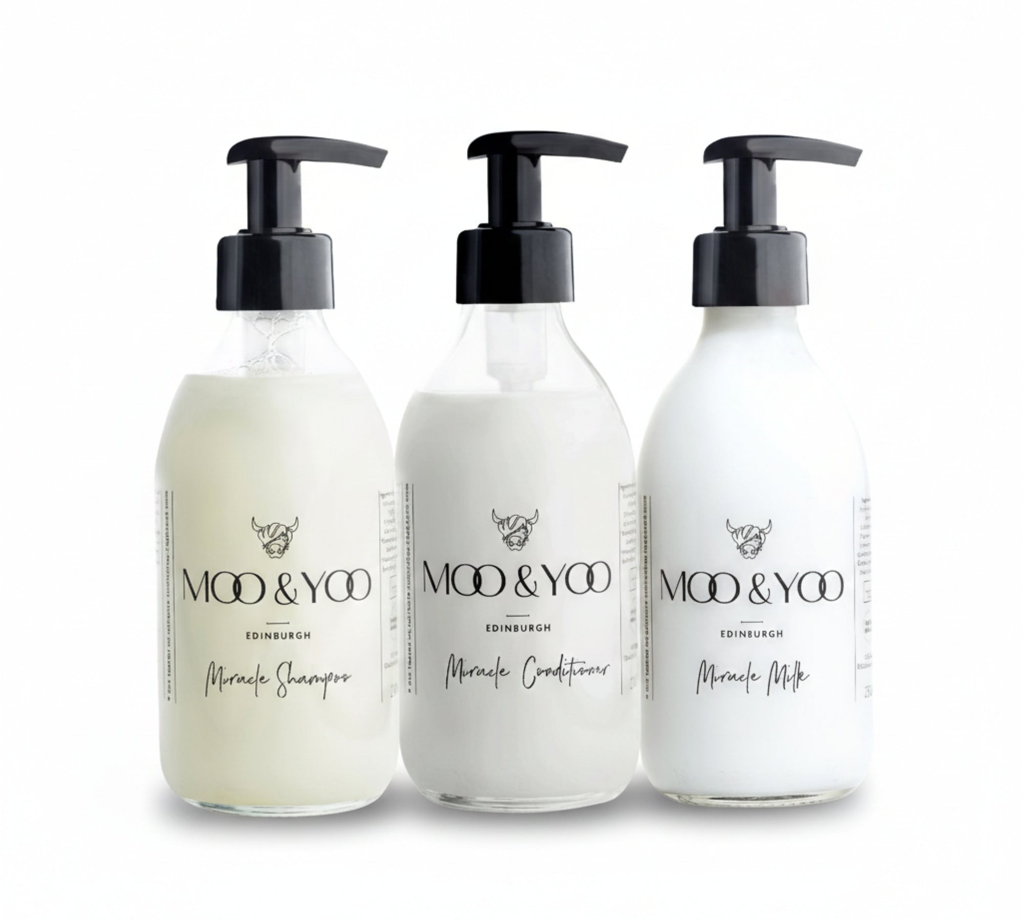 Three glass bottles of Moo and Yoo products sitting side by side. It is a Miracle Shampoo, Conditioner and Miracle Milk leave-in conditioner. They are on a white background