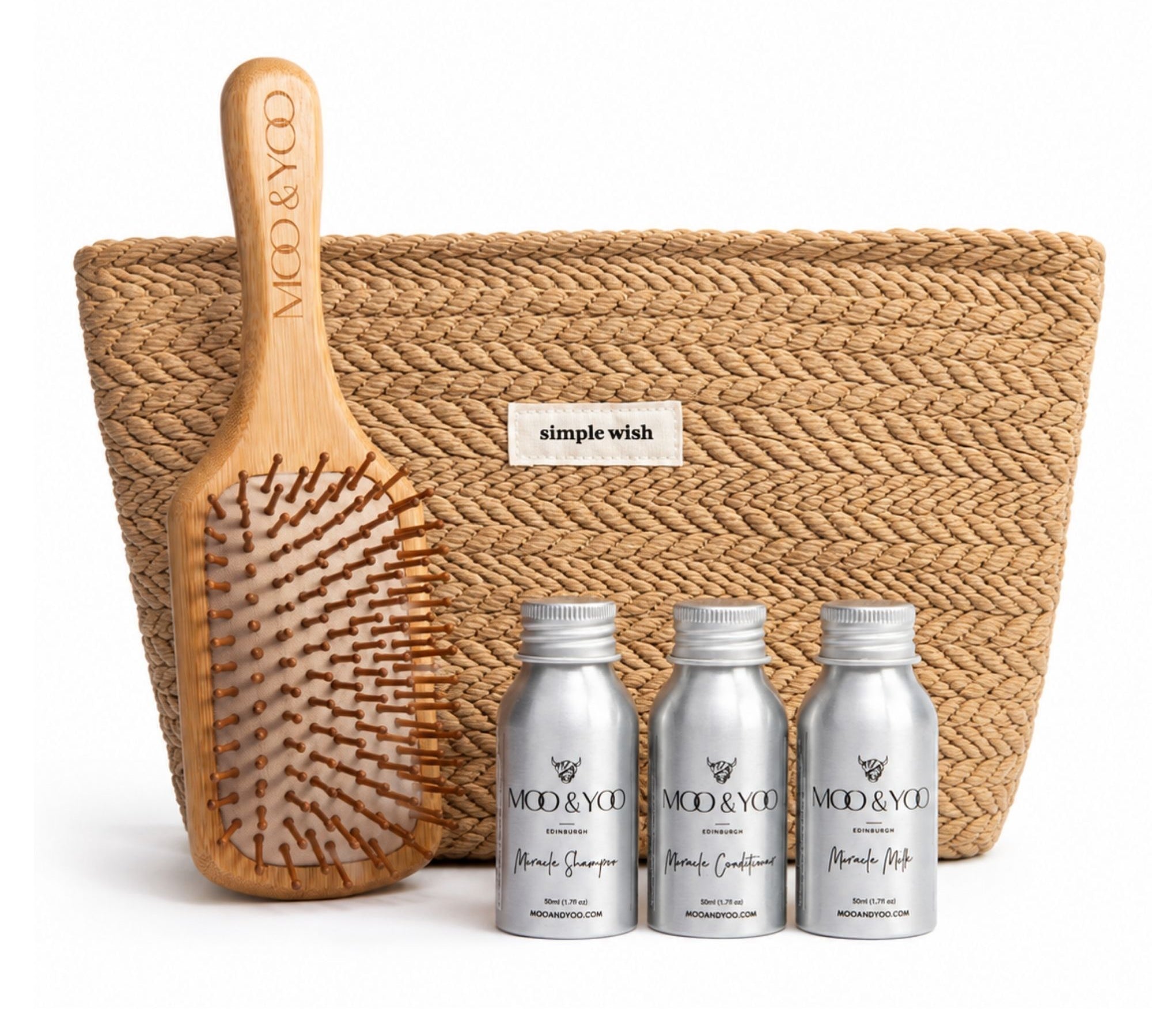 A hair care gift set from MOO & YOO featuring a natural woven pouch with a 'simple wish' label, a wooden paddle hairbrush engraved with the brand name, and three silver travel mini bottles of haircare products in the front.