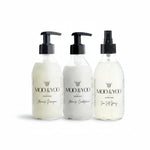 Three glass bottles of Moo and Yoo products sitting side by side. It is a Miracle Shampoo, Conditioner and a Sea Salt Spray. They are on a white background