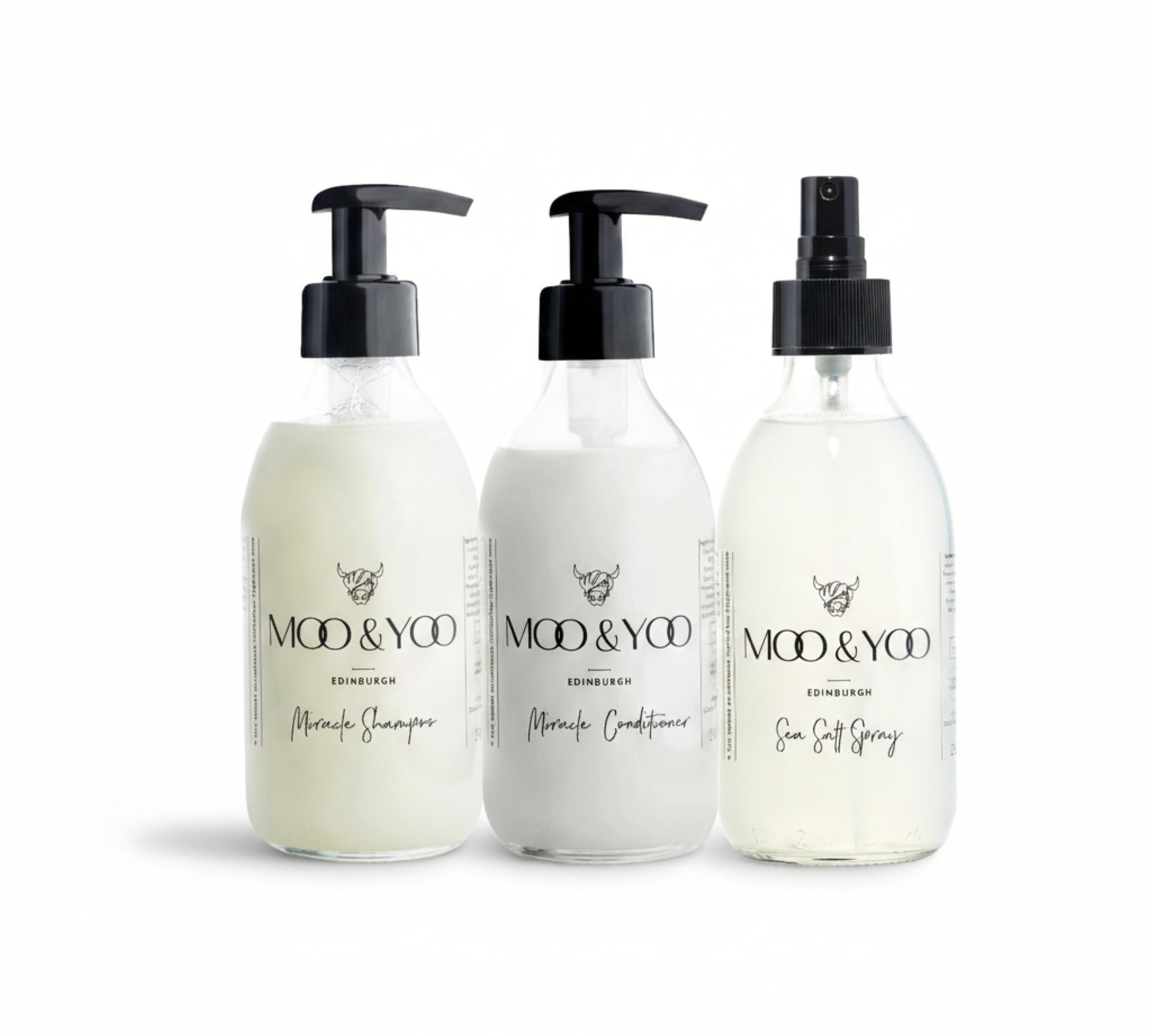 Three glass bottles of Moo and Yoo products sitting side by side. It is a Miracle Shampoo, Conditioner and a Sea Salt Spray. They are on a white background