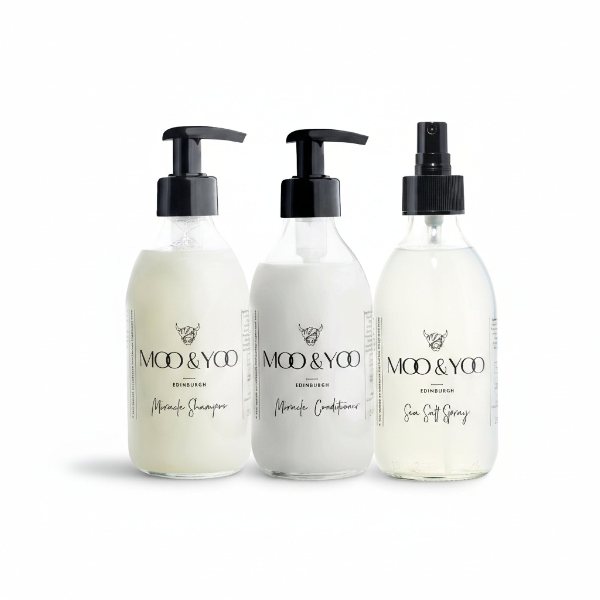 Three glass bottles of Moo and Yoo products sitting side by side. It is a Miracle Shampoo, Conditioner and a Sea Salt Spray. They are on a white background