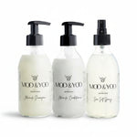 Three glass bottles of Moo and Yoo products sitting side by side. It is a Miracle Shampoo, Conditioner and a Sea Salt Spray. They are on a white background