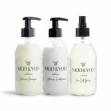 Three glass bottles of Moo and Yoo products sitting side by side. It is a Miracle Shampoo, Conditioner and a Sea Salt Spray. They are on a white background