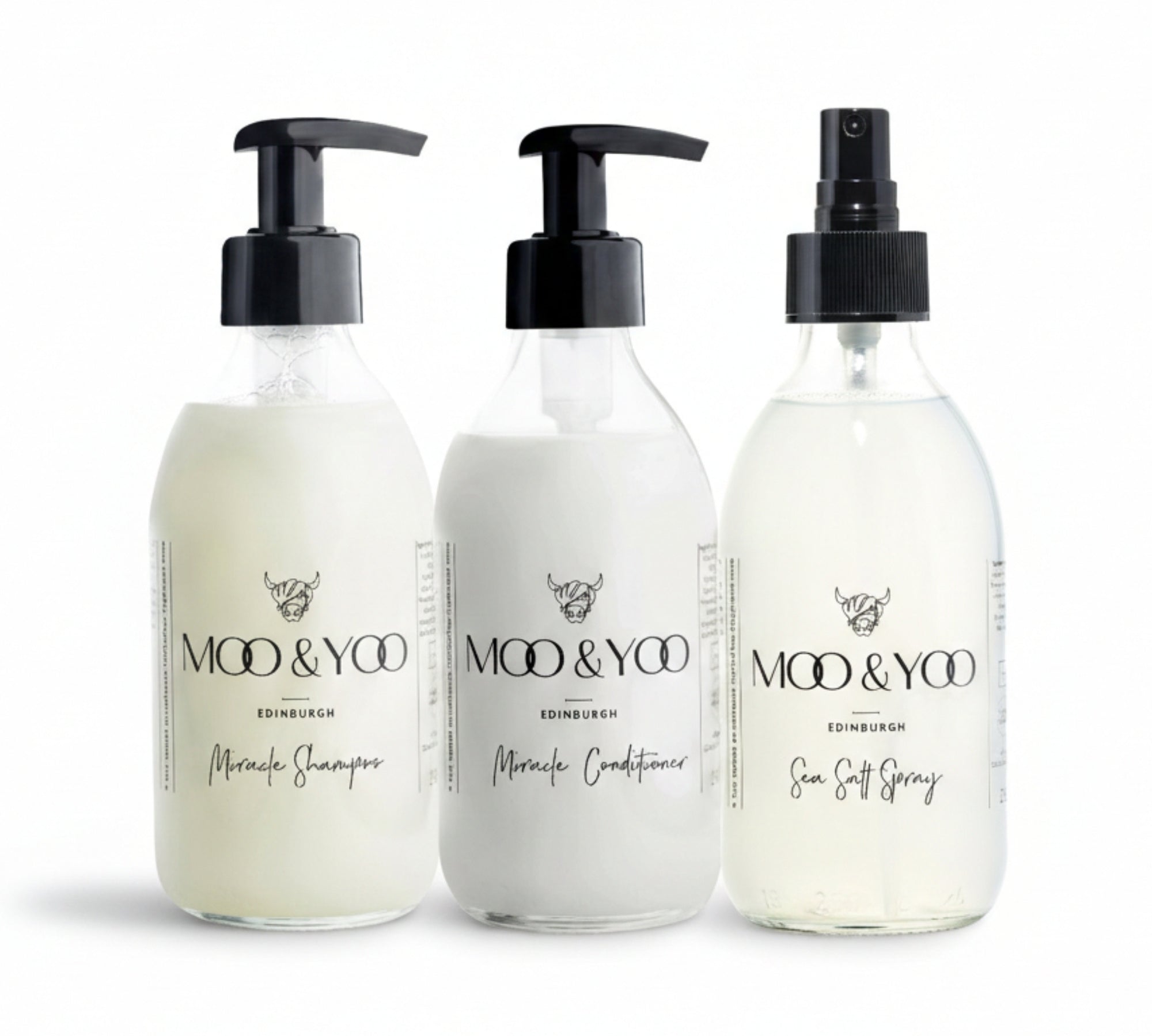 Three glass bottles of Moo and Yoo products sitting side by side. It is a Miracle Shampoo, Conditioner and a Sea Salt Spray. They are on a white background