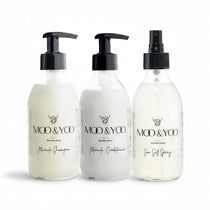 Three glass bottles of Moo and Yoo products sitting side by side. It is a Miracle Shampoo, Conditioner and a Sea Salt Spray. They are on a white background