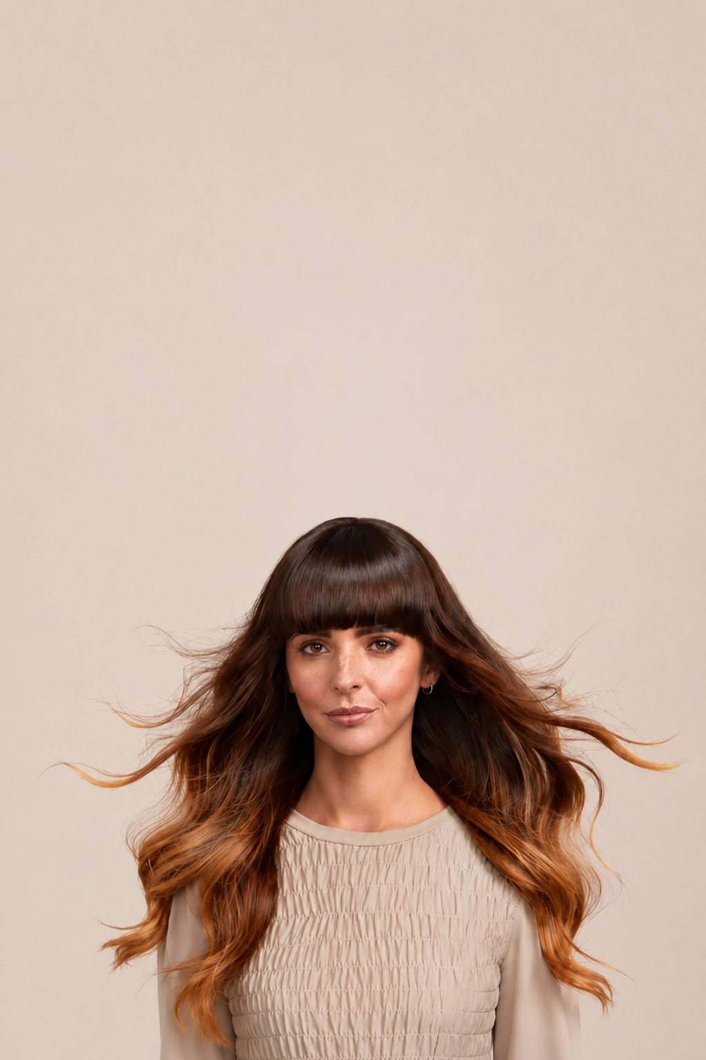 Model with long, glossy brunette hair against a soft taupe background, showcasing healthy, salon-finished hair.