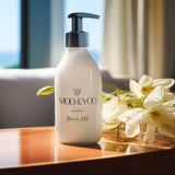 A glass bottle of Moo and Yoo Miracle Milk with a pump. It is placed on a table in a hotel suite. There is a bunch of white flowers laid down to the side.