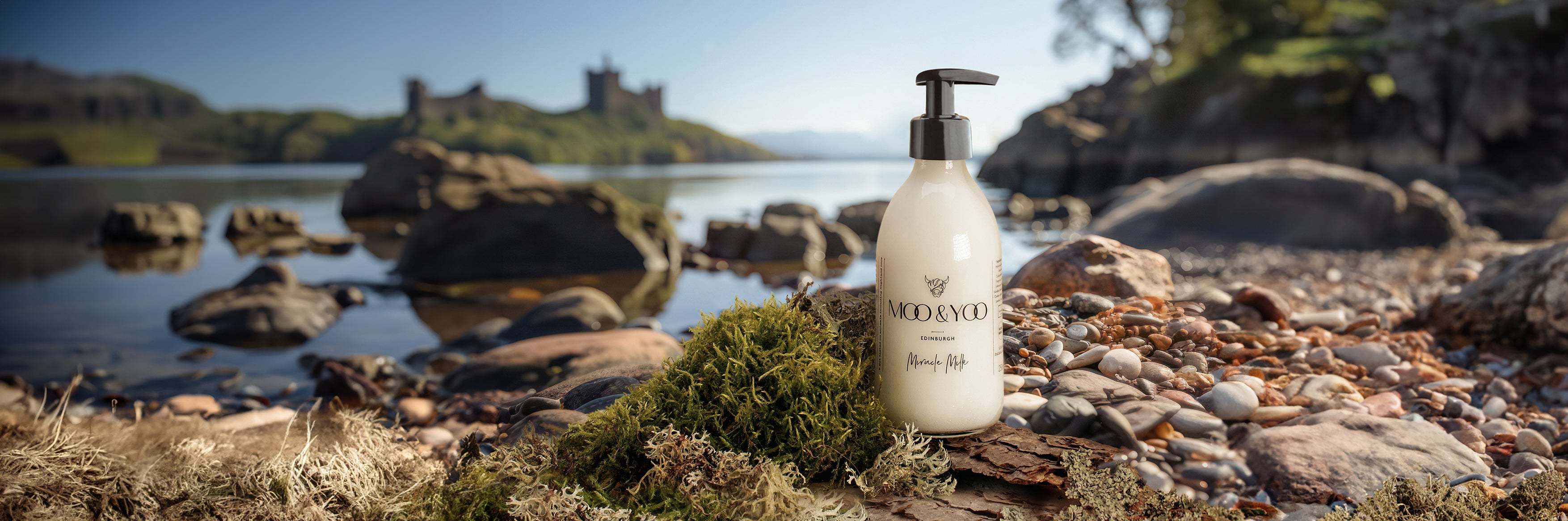 Our miracle milk in a glass bottle on cobblestones in the foreground with a lock and a Scottish castle in the background 