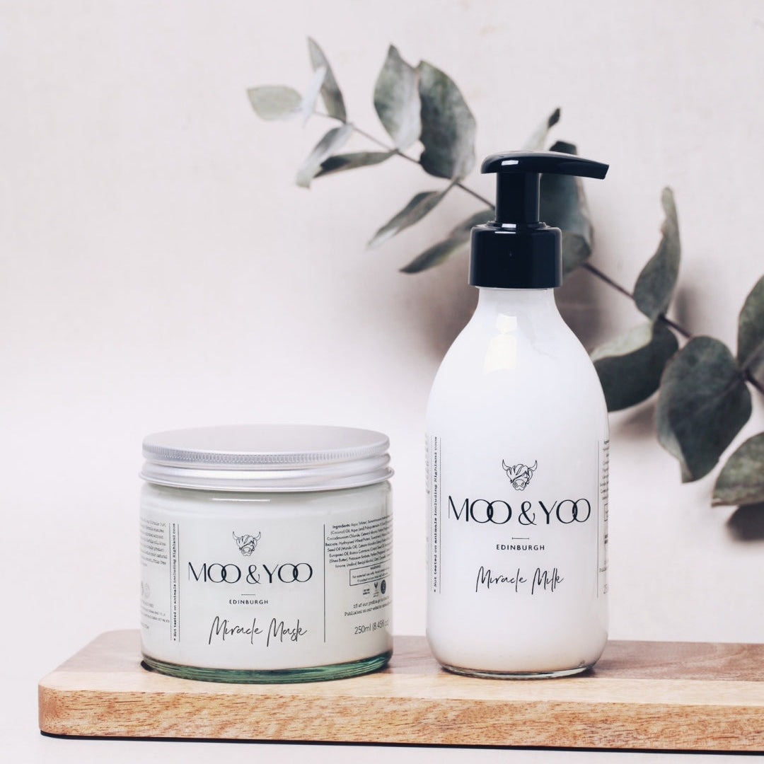 Two skincare products from the brand 'Moo & Yoo' on a wooden board with a light background and green leaves.