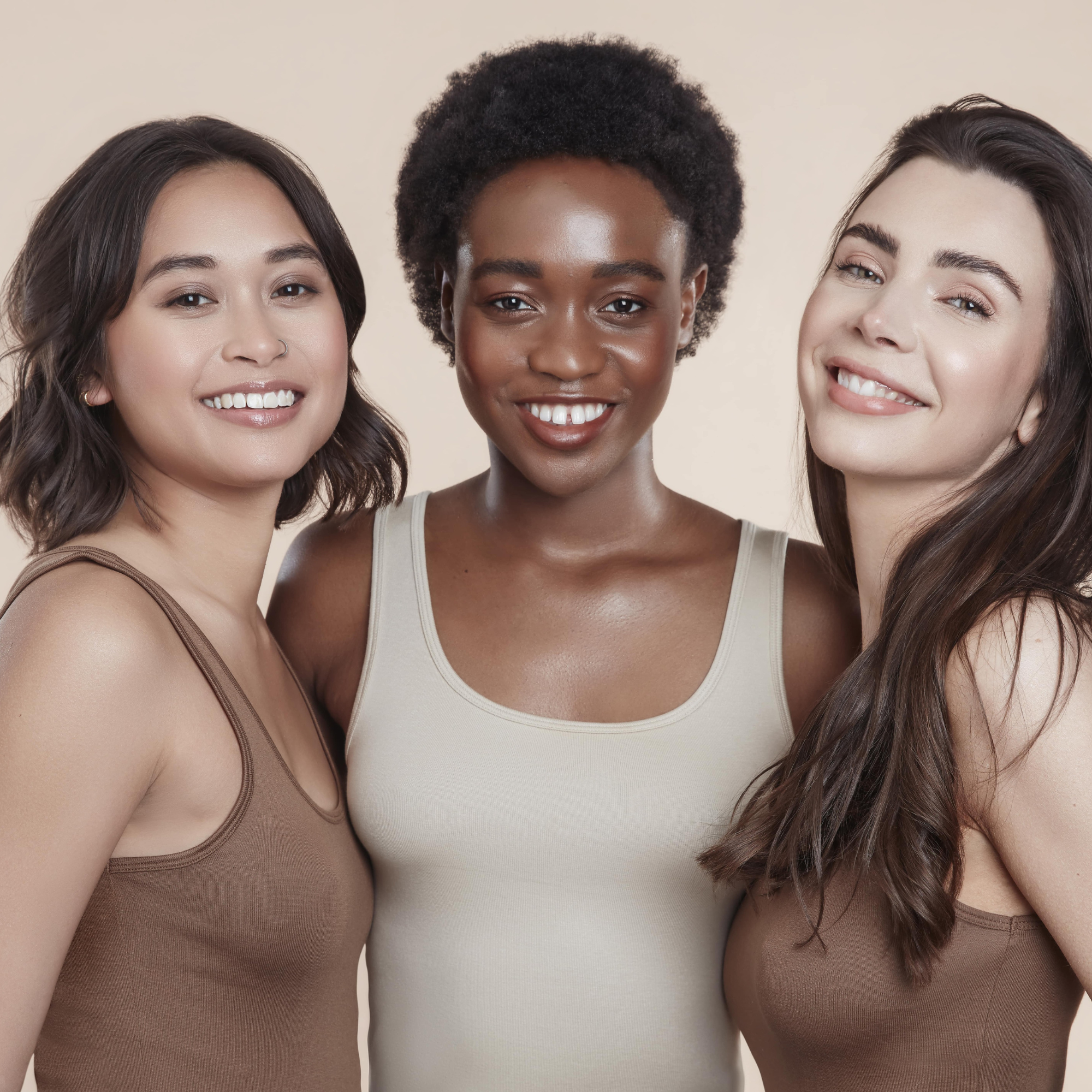 Image of three female models all looking at the camera. One has bob hair, the centre one has black textured natural hair and the thrid has long brunette hair. They are wearing neutral vest tops. Their skin is glowing and thier hair is healthy and shiny.
