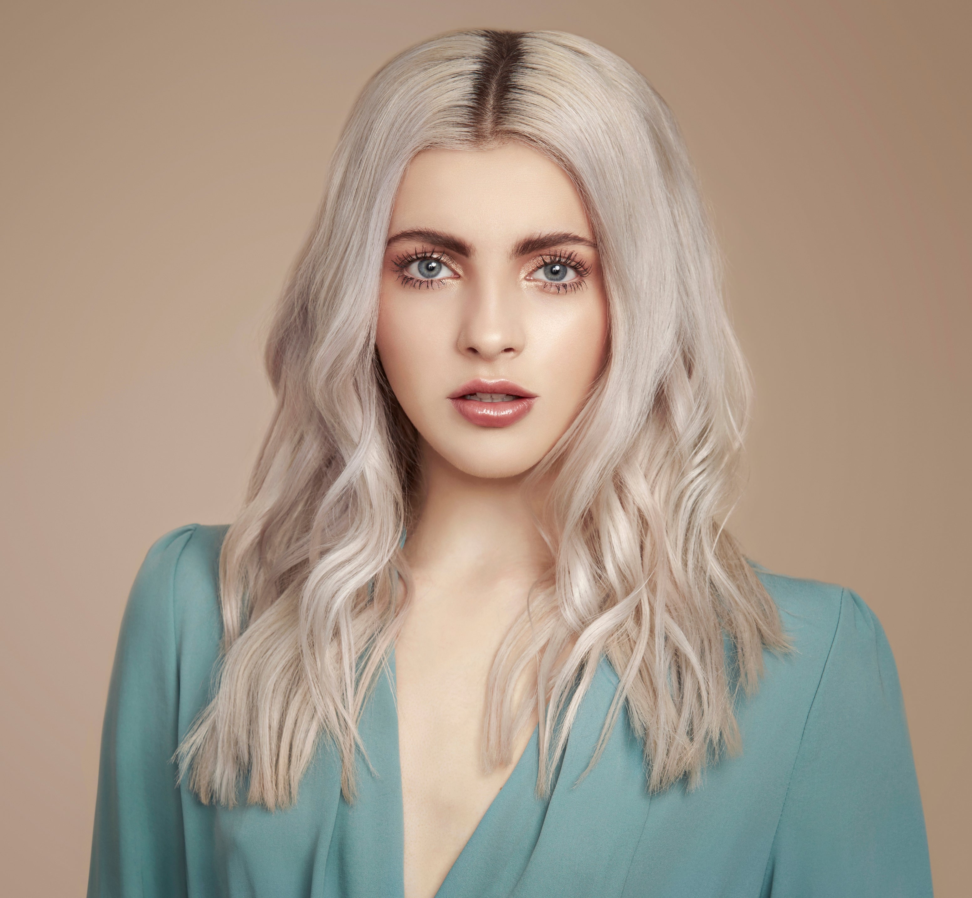 girl with bleach blonde hair in loose waves looking directly at the camera. She is pale with bright blue eyes matching her teal blue top