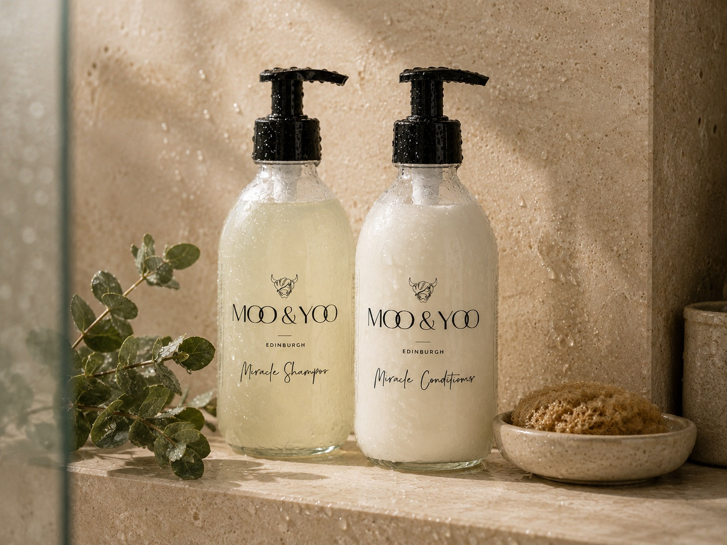 Moo & Yoo Miracle Shampoo and Conditioner in glass bottles displayed in a natural stone shower setting.