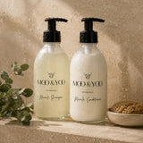 Moo & Yoo Miracle Shampoo and Conditioner in glass bottles displayed in a natural stone shower setting.