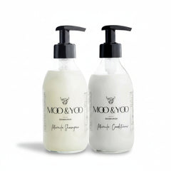 A glass bottle of Moo and Yoo Miracle Conditioner and a glass bottle of Moo and Yoo Miracle Shampoo sitting side by side with pumps on a white background 
