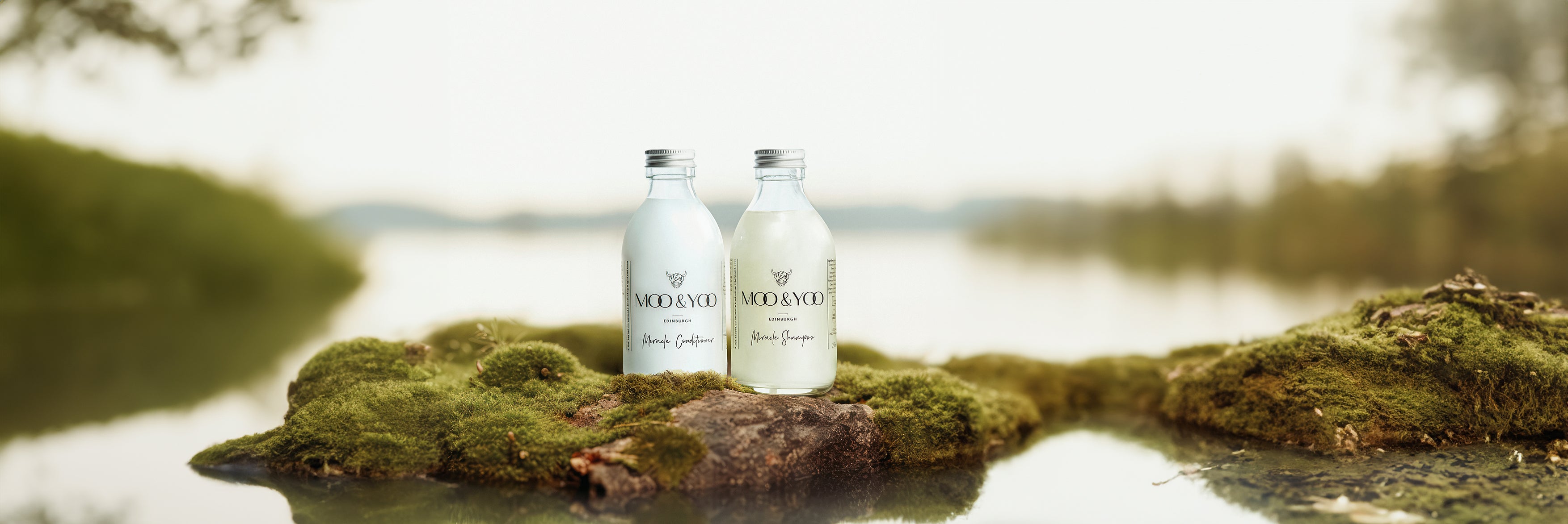 Our rituals duo of shampoo and conditioner in glass bottles on a moss island in the middle of a lake 