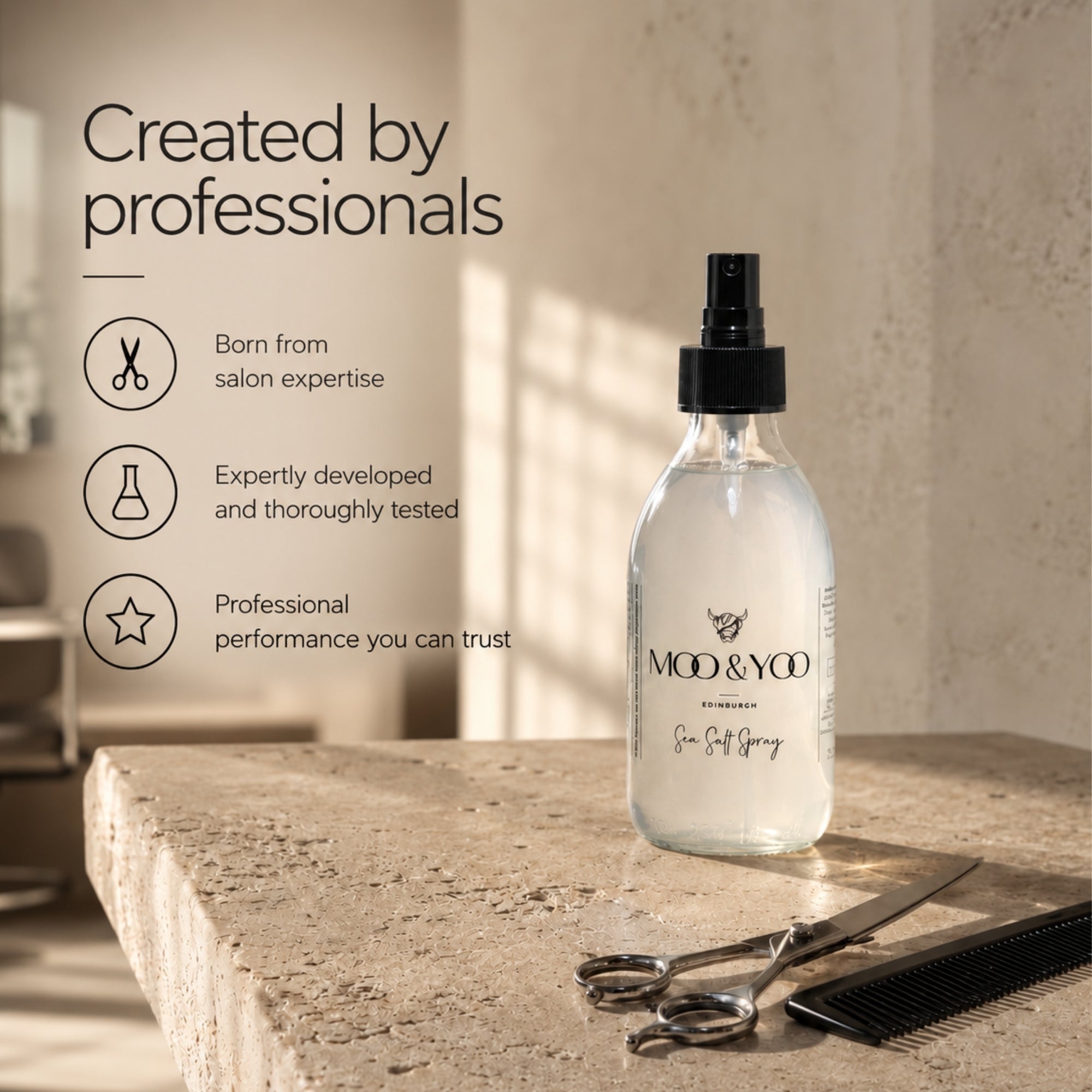 A clear glass spray bottle labeled 'MOD & YOOO Edinburgh Sea Salt Spray' stands on a stone surface in a warm, sunlit salon-like setting. Scissors and a comb rest nearby, with promotional text on the left reading 'Created by professionals.