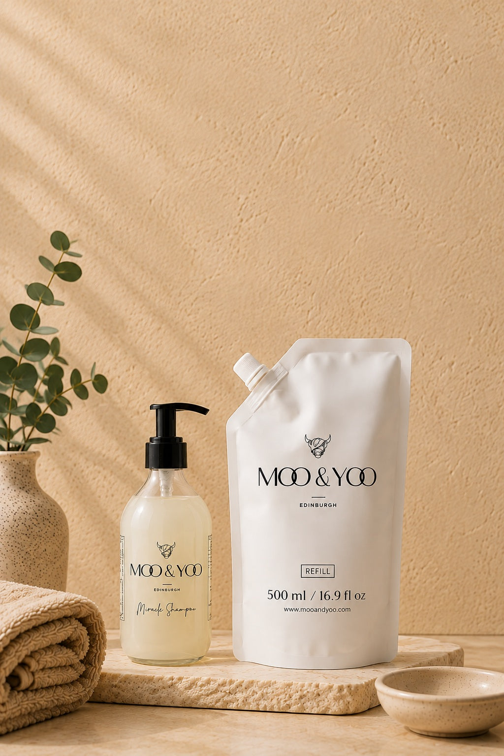Moo & Yoo Miracle Shampoo with 500ml refill pouch displayed on a natural stone tray with soft towels and eucalyptus in a warm, spa-inspired setting."