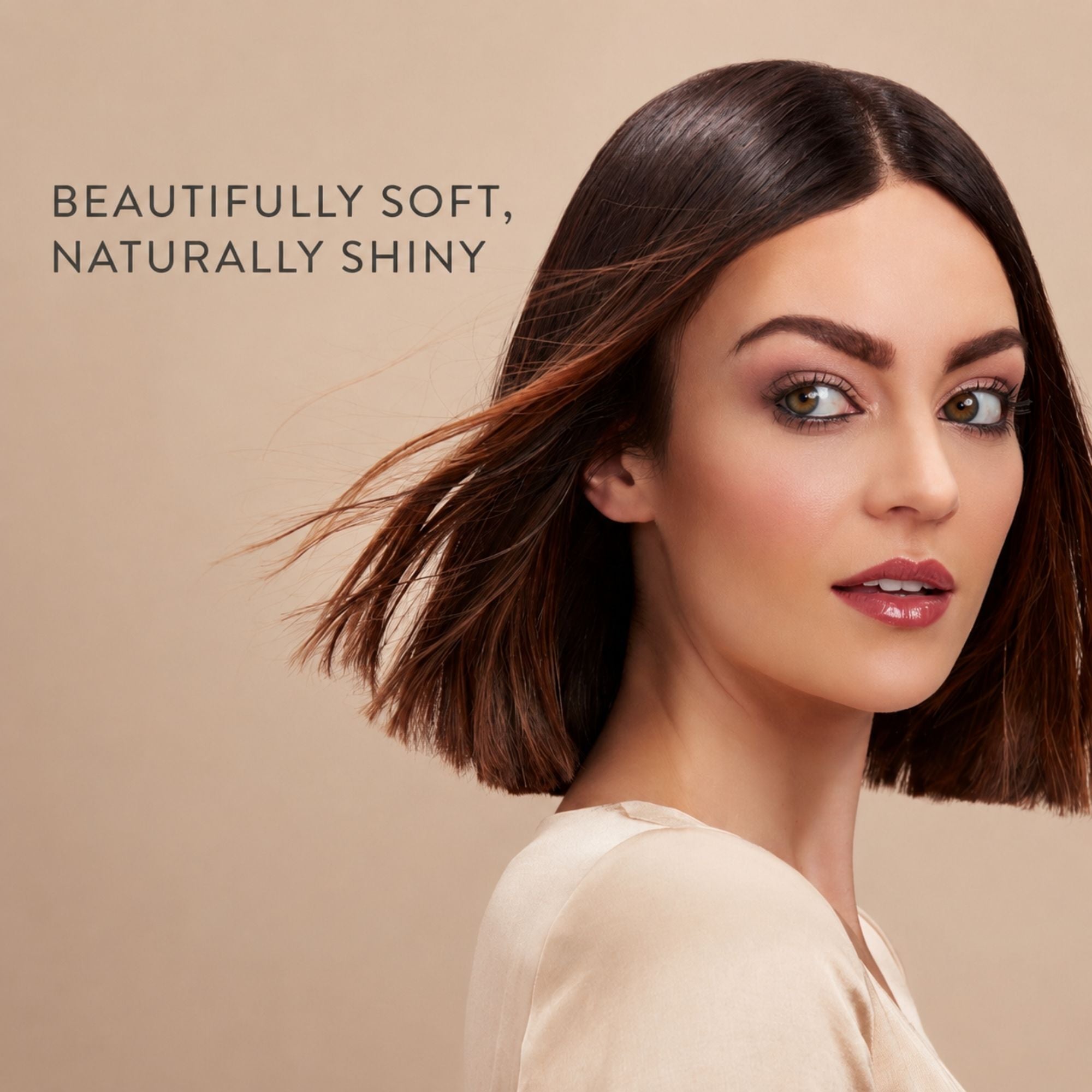 A woman with a shoulder-length dark brown bob haircut and glossy, soft-looking hair is shown against a warm beige background. Text on the left reads, 'BEAUTIFULLY SOFT, NATURALLY SHINY.