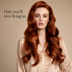 A woman with long, wavy auburn-red hair wearing a light beige satin blouse, posed against a warm beige background with the text 'Hair you'll love living in.' on the left.