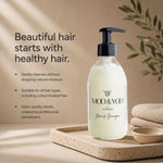 MOO & YOO Edinburgh Miracle Shampoo in a frosted glass pump bottle, displayed on a stone tray with folded linen and a small bowl against a warm beige background with text describing hair care benefits.
