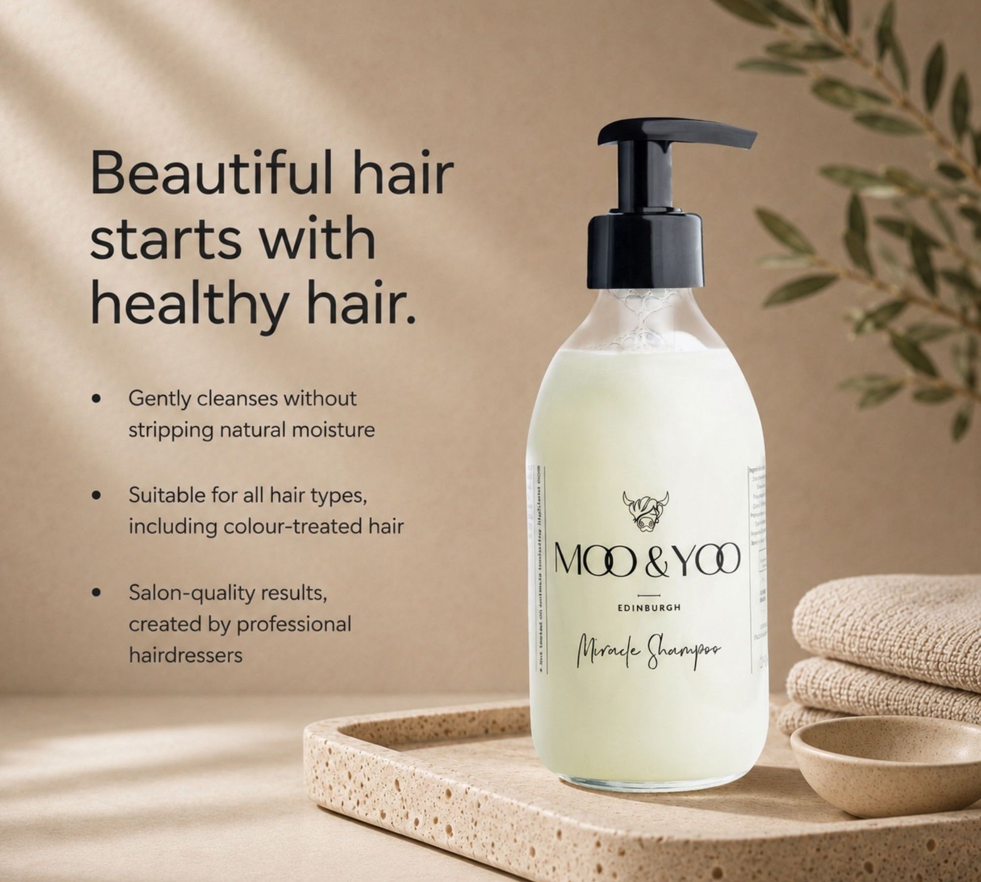 MOO & YOO Edinburgh Miracle Shampoo in a frosted glass pump bottle, displayed on a stone tray with folded linen and a small bowl against a warm beige background with text describing hair care benefits.
