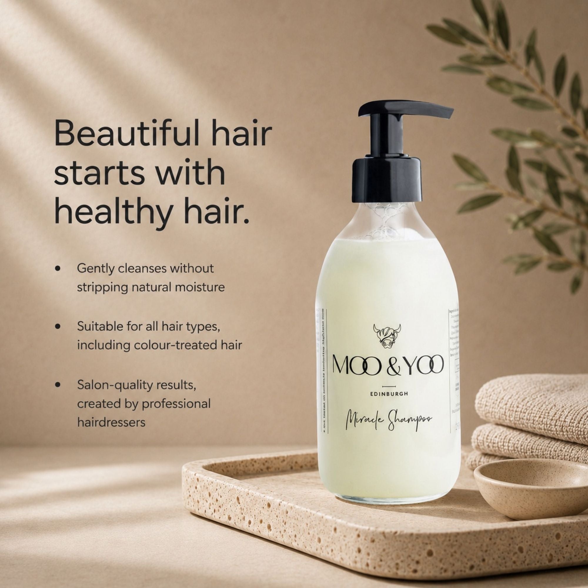 MOO & YOO Edinburgh Miracle Shampoo in a frosted glass pump bottle, displayed on a stone tray with folded linen and a small bowl against a warm beige background with text describing hair care benefits.