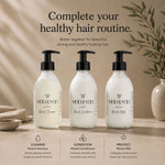 Three bottles of Moo and Yoo hair care products lined up on a beige surface: Miracle Shampoo, Miracle Conditioner, and Miracle Milk. The bottles are clear with white liquid and black pumps, set against a warm neutral background with text and small decorative props.