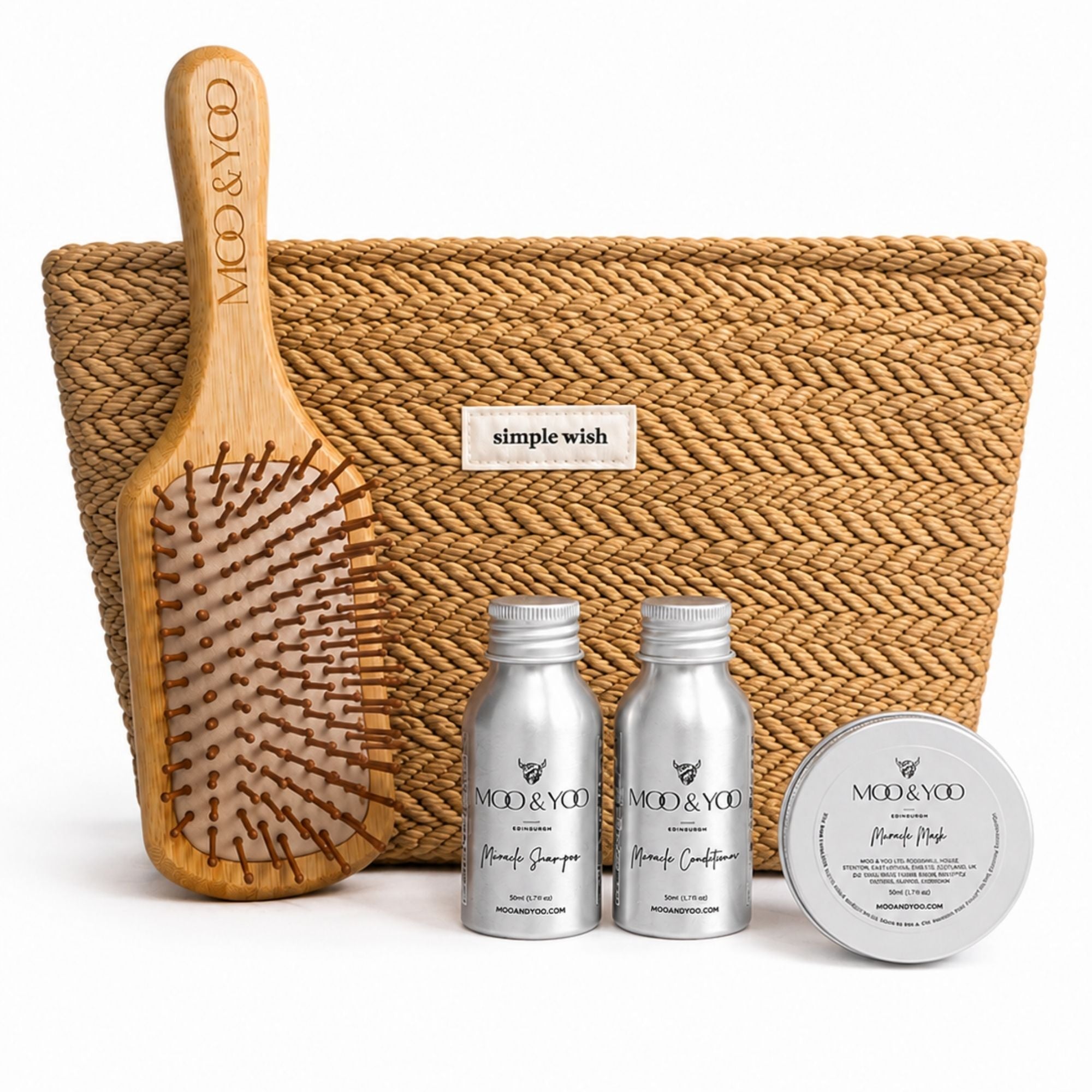 A hair care gift set from MOO & YOO featuring a natural woven pouch with a 'simple wish' label, a wooden paddle hairbrush engraved with the brand name, and three silver travel mini bottles and tins of haircare products in the front.