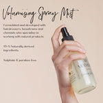 Hand holding a volumising spray mist bottle with product details on a beige background