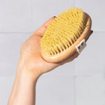 Hand holding a natural bristle brush against a white tile bathroom background