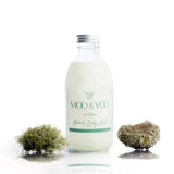 Glass bottle of Miracle Body Wash with an aluminium lid on a white background with a sprig of moss on each side.