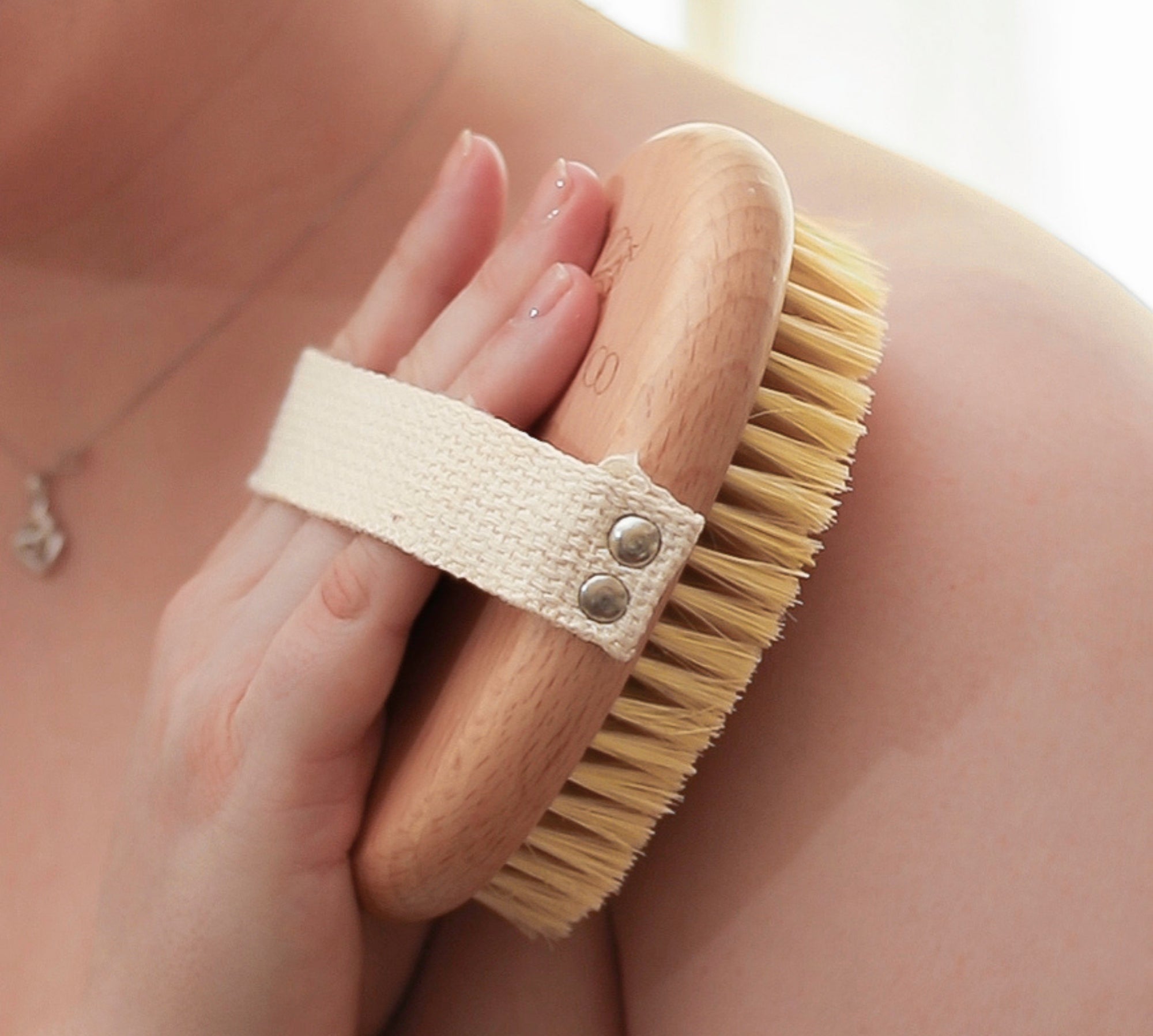 Person using a wooden body brush with natural bristles on their shoulder.