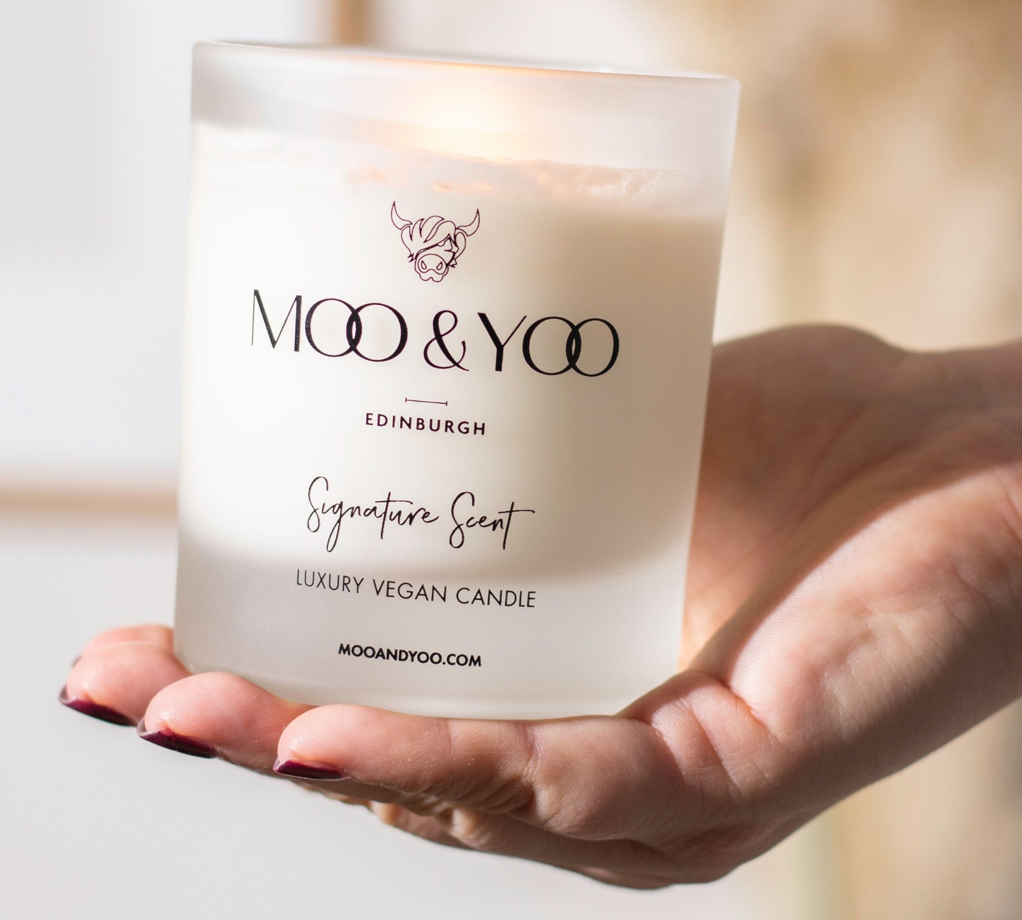 Hand holding a MOO & YOO candle with a blurred background