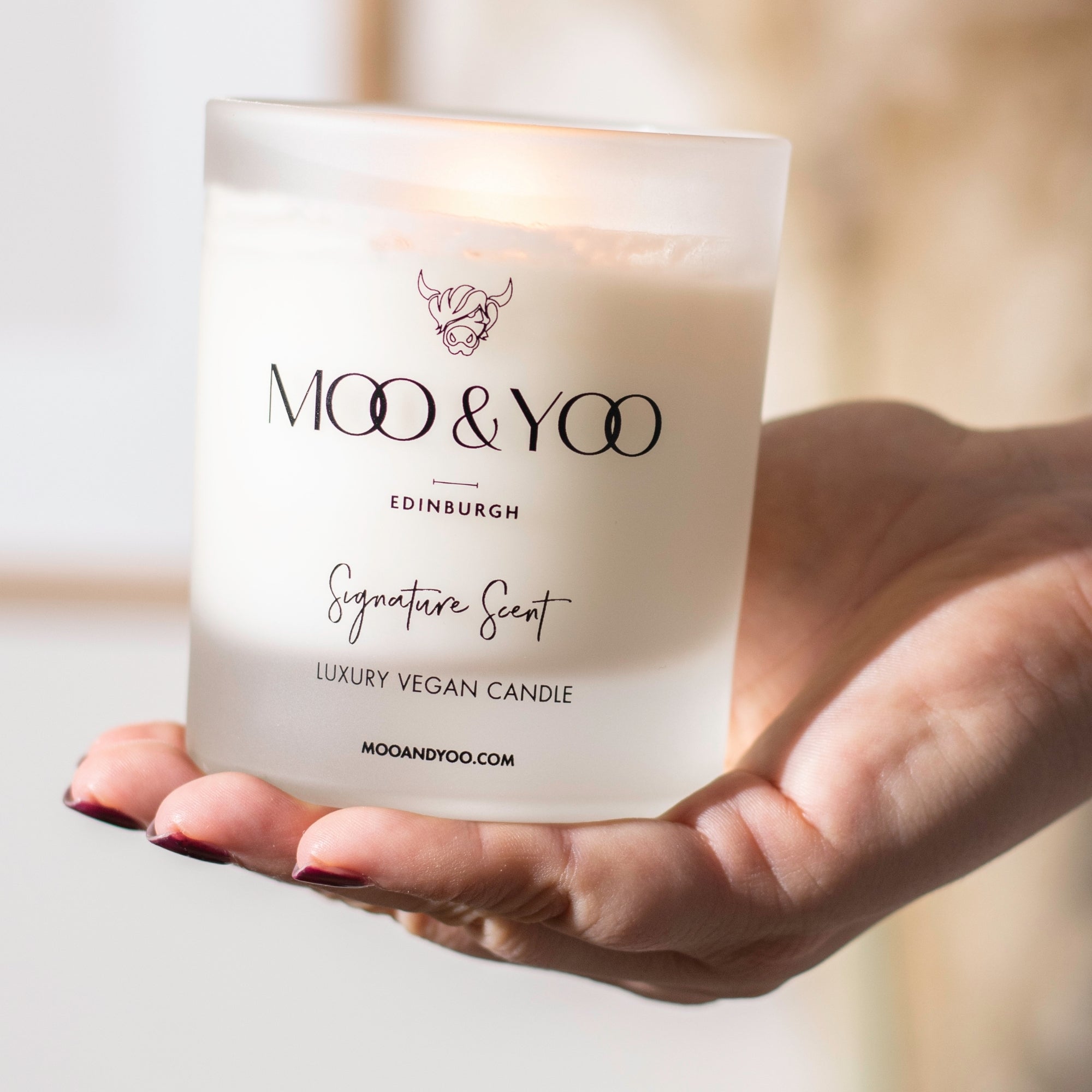 Hand holding a MOO & YOO candle with a blurred background
