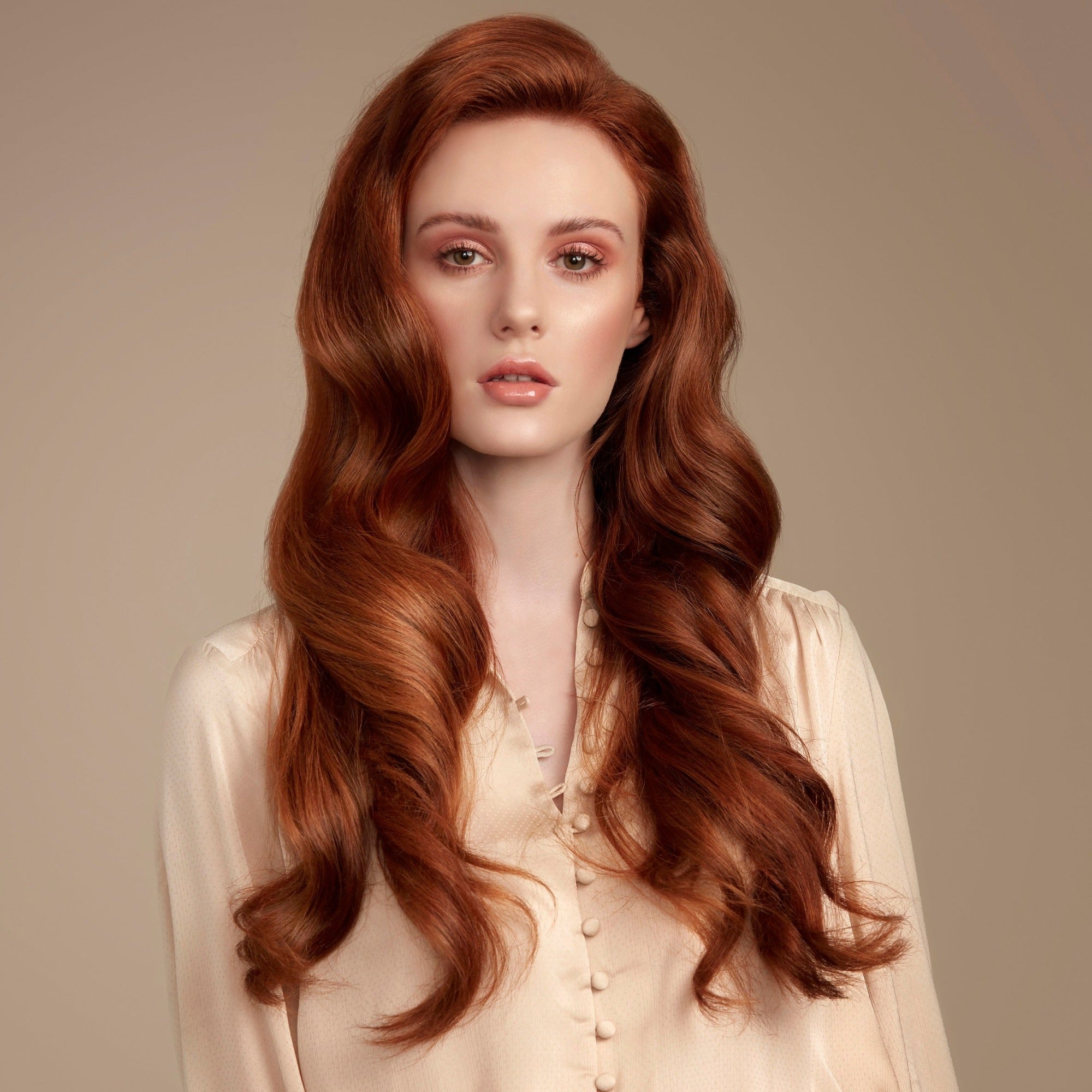 Female model with flowing long red wavy hair. She has a pale champagne coloured top. She is looking directly at the camera.. She has super shiny long wavy hair with lots of volume from a weekly use of Moo and Yoo Mask.