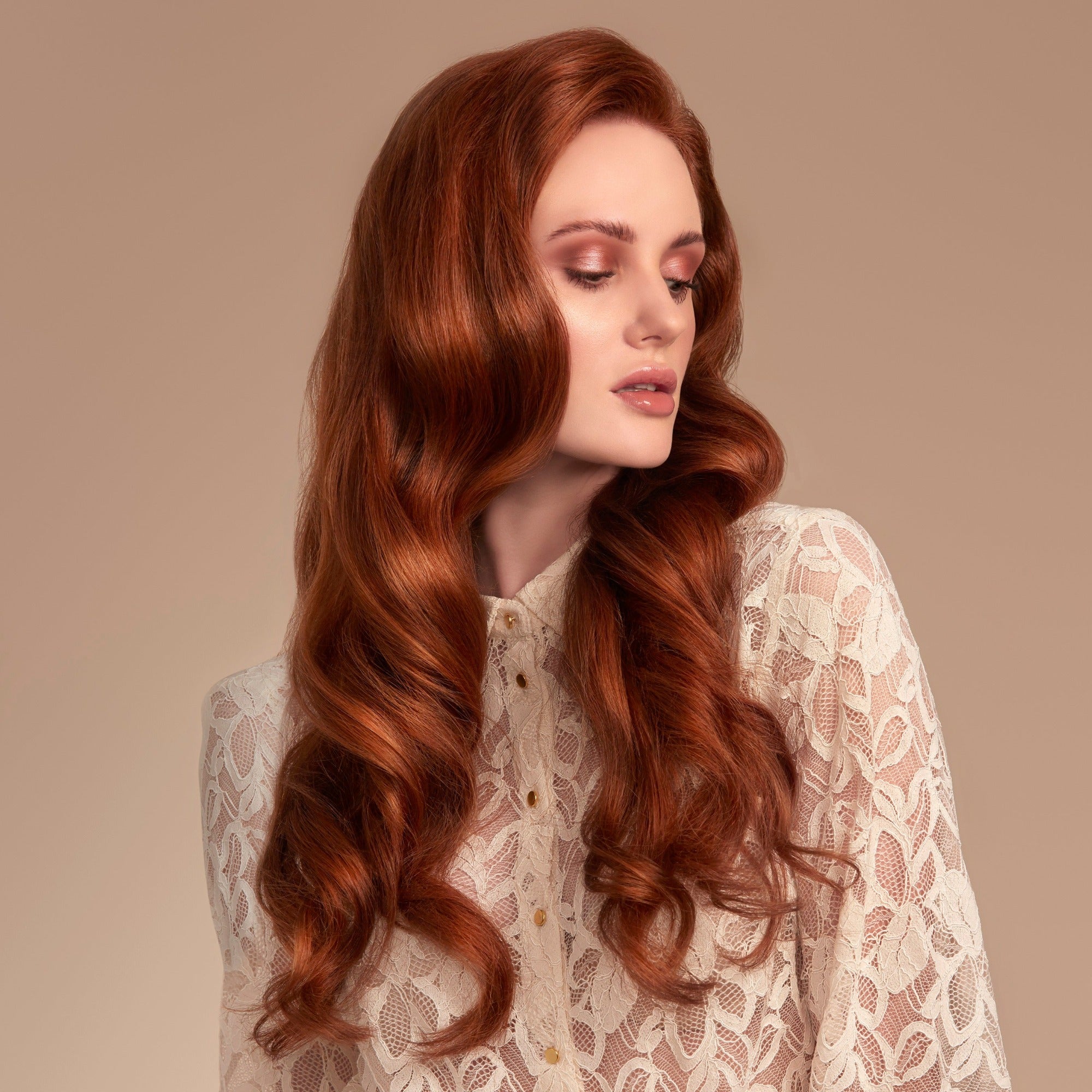 Female model with flowing long red wavy hair from using Moo and Yoo Miracle Shampoo and Conditioner and a weekly Miracle hair mask. She has a pale cream lacey top on. She is looking to the right so you can see the full side of her hair. She has super shiny long wavy hair using Moo and Yoo conditioner with lots of volume.