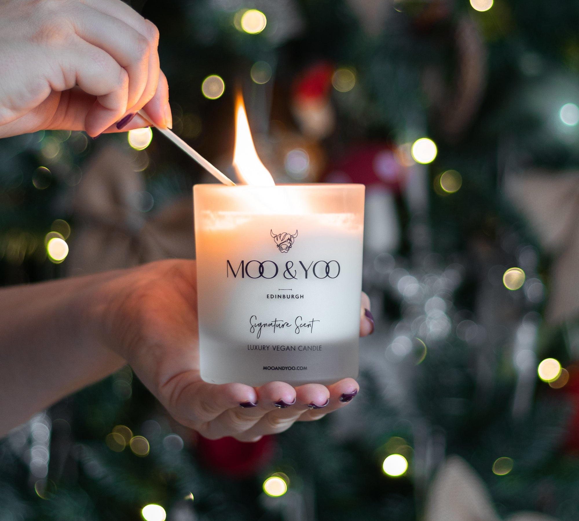 Person lighting a MOO & YOO candle with a Christmas tree in the background