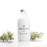 A glass bottle of Moo and Yoo Miracle conditioner with an aluminium lid on a white background with a sprig of Icelandic moss placed to each side.