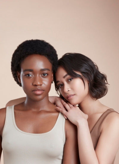 two girls one on left facing front with short cropped black afro textured hair and girl on right leaning on her shoulder facing forward with short choppy wavy hair 