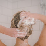Person washing her hair with moo & yoo miracle shampoo in a bathroom setting