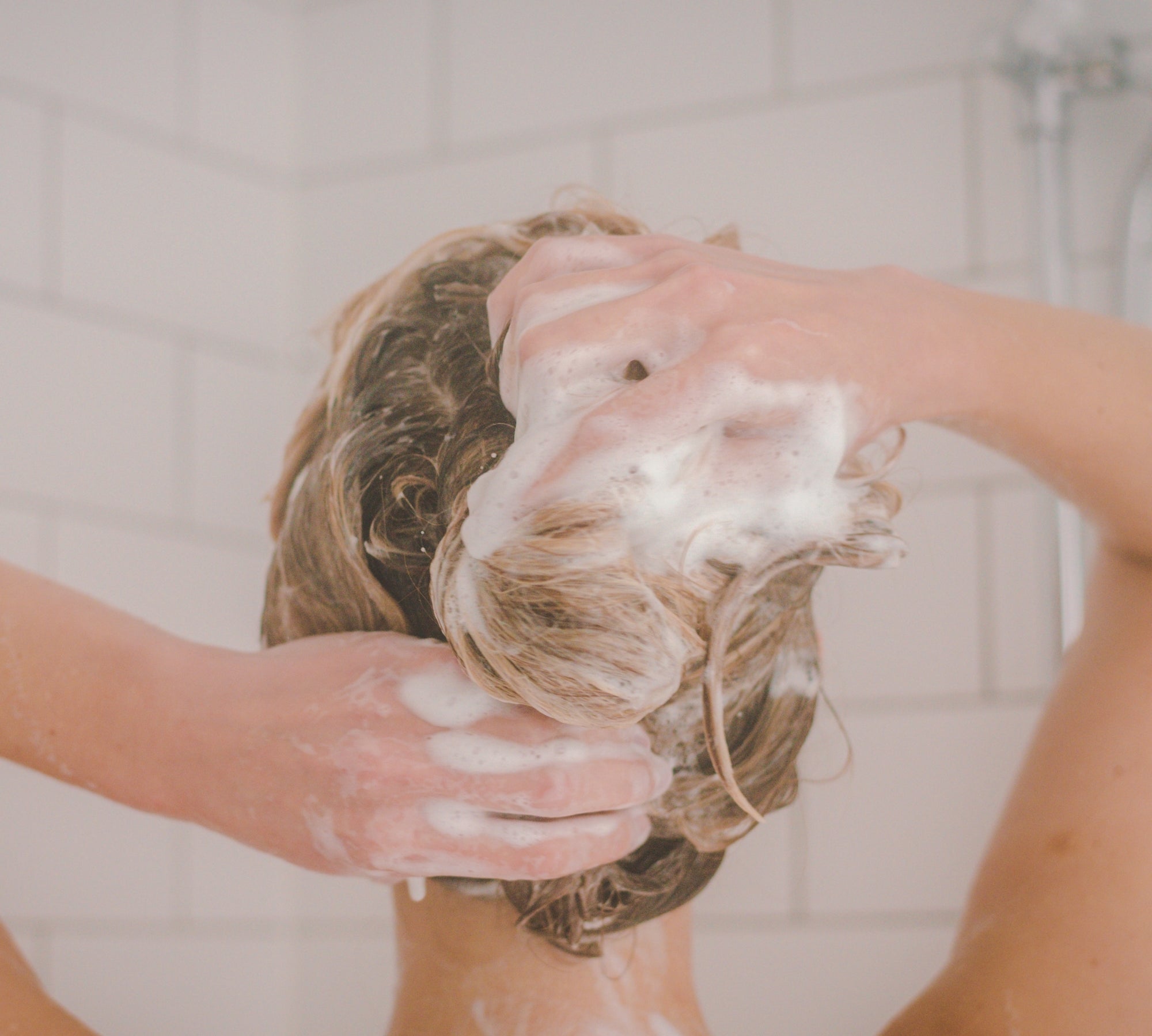 Person washing her hair with moo & yoo miracle shampoo in a bathroom setting