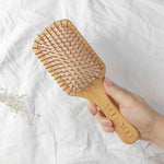 Wooden hairbrush held by a hand on a white sheet background