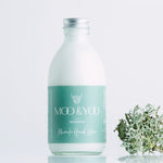 Glass bottle of Miracle Hand Lotion on a white background with a sprig of moss to each side.