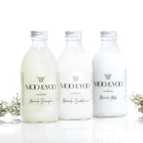 Three glass bottles of Moo and Yoo products sitting side by side. It is a Miracle Shampoo, Conditioner and a Volumising Spray Mist. All have aluminium lids.  They are on a white background with a sprig of Icelandic moss placed to each side.