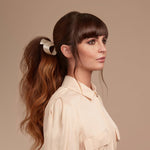 Female model with long wavy brunette hair tied into a low pony tail with a cream ribbon.  Her hair is very shiny from using Moo and Yoo Miracle Conditioner, Mircle Milk and Mask. She is wearing a simple white dress with black trim.